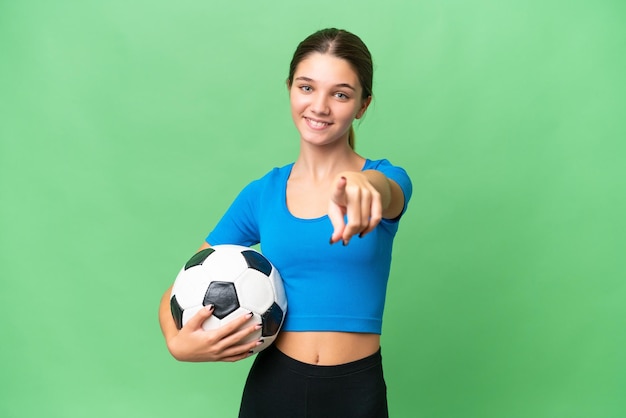 Menina caucasiana adolescente jogando futebol sobre fundo isolado aponta o dedo para você com uma expressão confiante