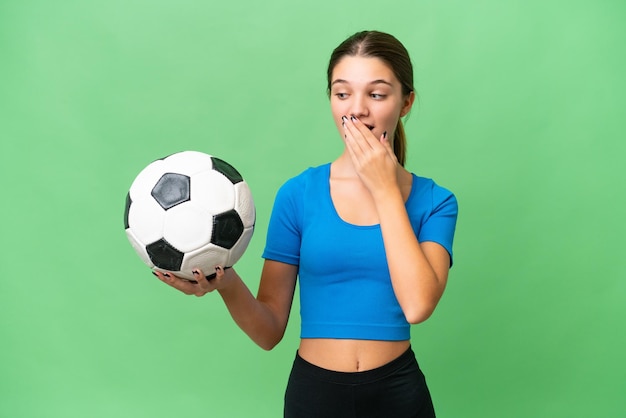 Menina caucasiana adolescente jogando futebol sobre fundo isolado com surpresa e expressão facial chocada