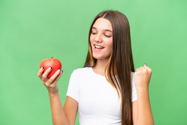 Menina caucasiana adolescente segurando uma maçã sobre fundo isolado comemorando uma vitória