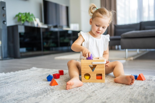 Menina caucasiana bonitinha brincando no chão em casa com brinquedos ecológicos de madeira A criança jogando jogos educativos