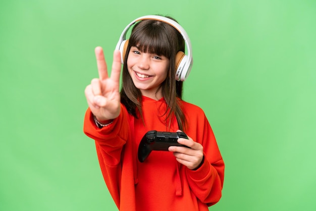 Menina caucasiana brincando com um controlador de videogame sobre fundo isolado sorrindo e mostrando sinal de vitória