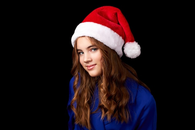 Menina caucasiana com cabelo comprido em vestido azul usando chapéu de papai noel isolado em fundo preto