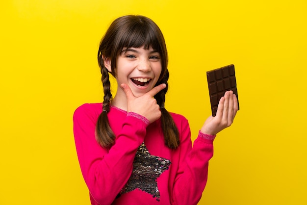 Menina caucasiana com chocolate isolado em fundo amarelo feliz e sorridente