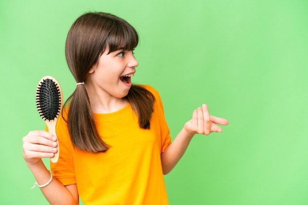 Foto menina caucasiana com pente de cabelo sobre fundo isolado com expressão facial de surpresa