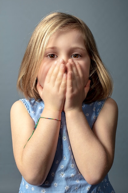 Foto menina caucasiana de 5 anos de idade com as mãos cobrindo o rosto.