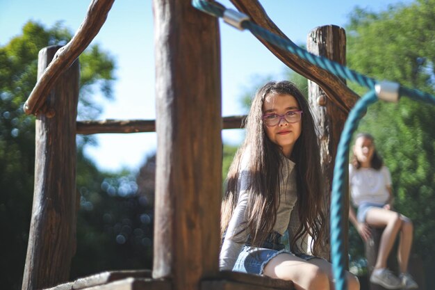 Menina caucasiana de retrato senta-se em um balanço de corda olhando para a câmera em um parque em um playground