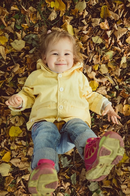 Menina caucasiana deitada nas folhas no parque outono e sorrindo