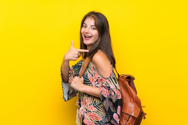 Menina caucasiana em vestido colorido isolado parede amarela com mochila