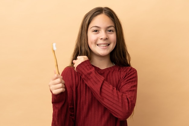 Menina caucasiana, escovando os dentes isolados em um fundo bege, comemorando uma vitória