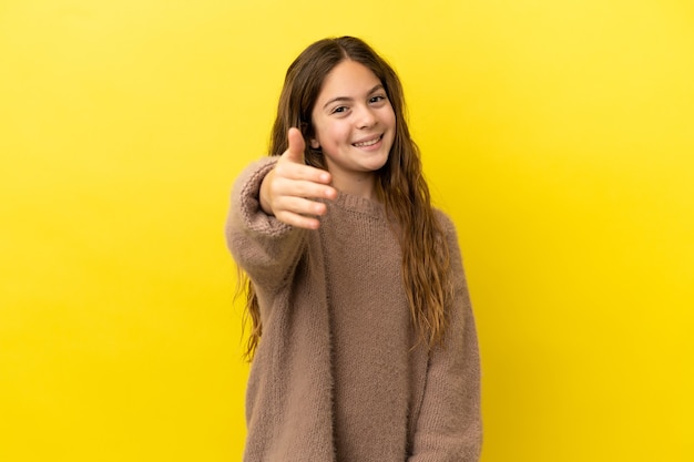 Foto menina caucasiana isolada em fundo amarelo apertando as mãos para fechar um bom negócio