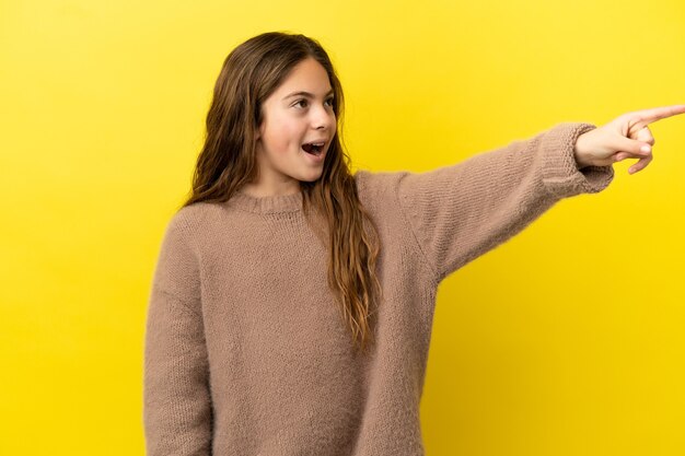 Menina caucasiana isolada em fundo amarelo apontando para longe