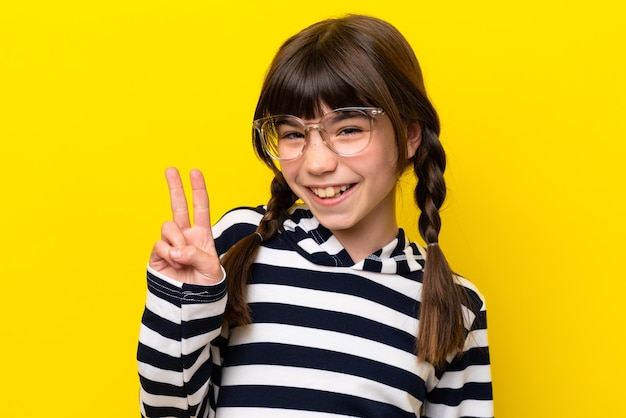 Menina caucasiana isolada em fundo amarelo com óculos e fazendo sinal de OK