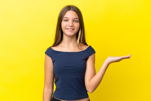 Menina caucasiana isolada em fundo amarelo segurando copyspace imaginário na palma da mão para inserir um anúncio