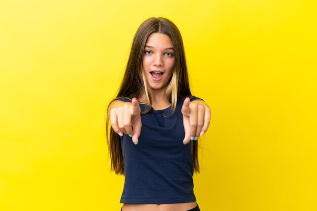 Menina caucasiana isolada em fundo amarelo surpreso e apontando para a frente