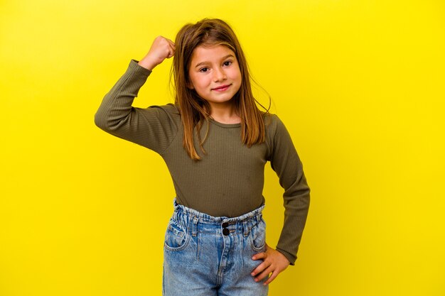 Menina caucasiana isolada em fundo amarelo torcendo despreocupada e animada. Conceito de vitória.