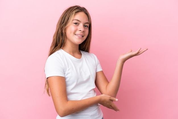 Menina caucasiana isolada em fundo rosa, estendendo as mãos para o lado para convidar para vir