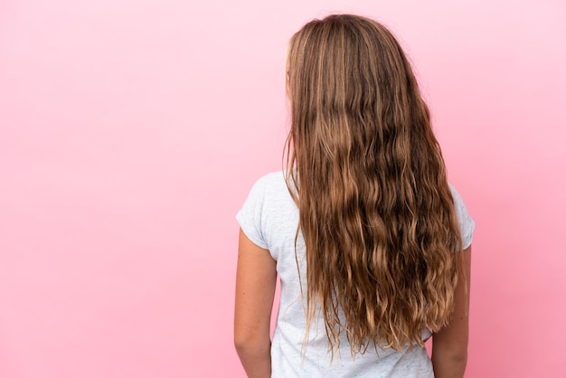 Menina caucasiana isolada em fundo rosa na posição traseira e olhando de lado