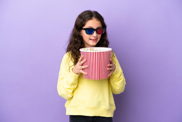 Menina caucasiana isolada em fundo roxo com óculos 3d e segurando um grande balde de pipocas