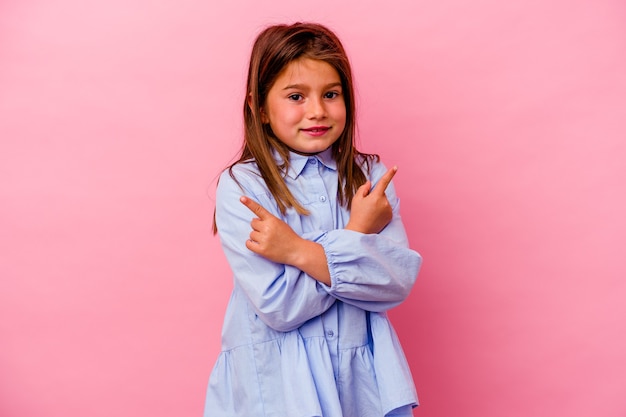 Menina caucasiana isolada em pontos de fundo rosa para os lados, está tentando escolher entre duas opções.