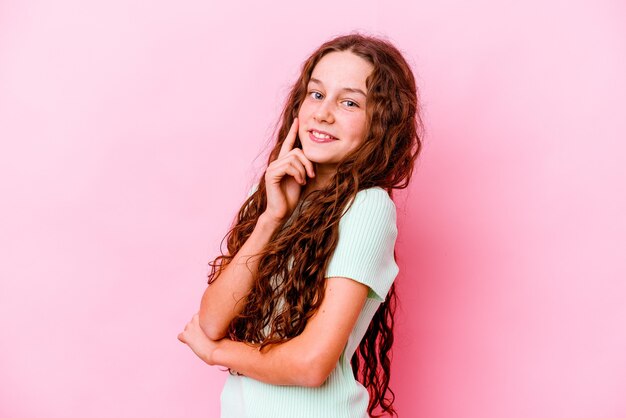 Menina caucasiana isolada em rosa sorrindo feliz e confiante, tocando o queixo com a mão.