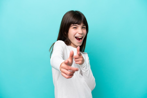 Menina caucasiana isolada em um fundo azul apontando para a frente e sorrindo