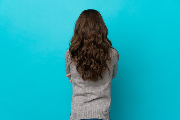 Menina caucasiana isolada em um fundo azul na posição traseira