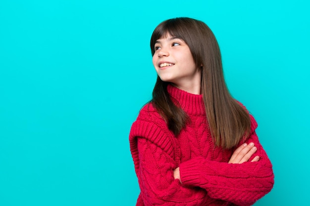 Menina caucasiana isolada em um fundo azul, olhando para o lado e sorrindo