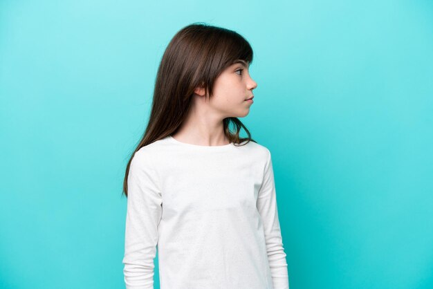 Menina caucasiana isolada em um fundo azul, olhando para o lado