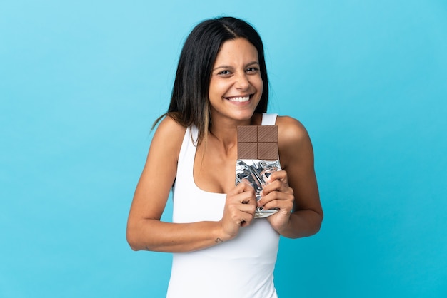 Menina caucasiana isolada em um fundo azul tomando uma pastilha de chocolate e feliz