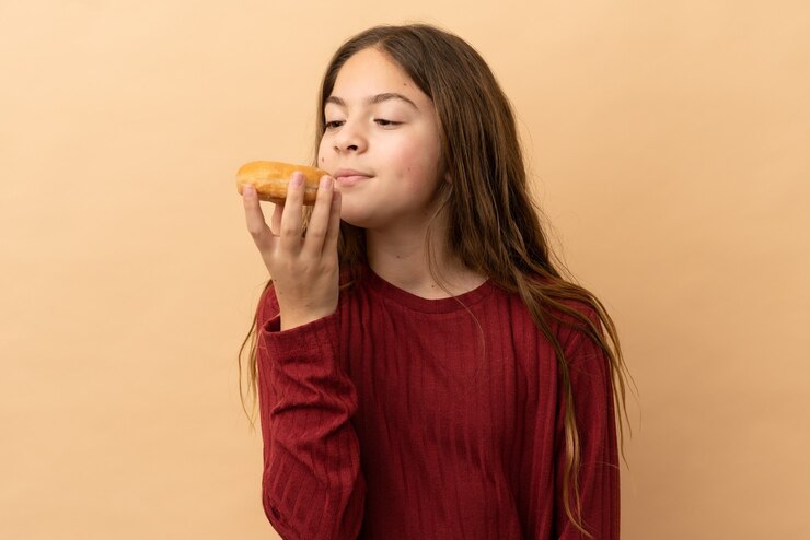 Foto menina caucasiana isolada em um fundo bege segurando rosquinhas com uma expressão feliz