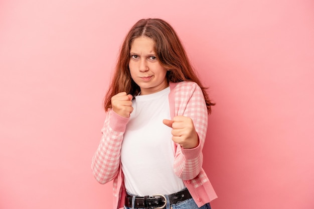 Menina caucasiana isolada em um fundo rosa, mostrando o punho para a câmera, expressão facial agressiva.