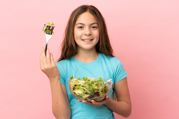 Menina caucasiana isolada em um fundo rosa segurando uma tigela de salada com uma expressão feliz