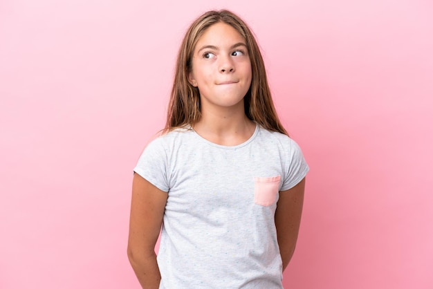 Menina caucasiana isolada em um fundo rosa tendo dúvidas enquanto olha para cima