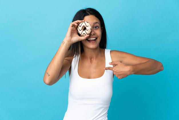 Menina caucasiana isolada na parede azul segurando um donut e feliz