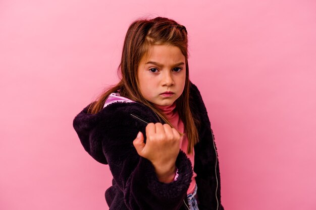 Menina caucasiana isolada na rosa mostrando o punho para a câmera, expressão facial agressiva.