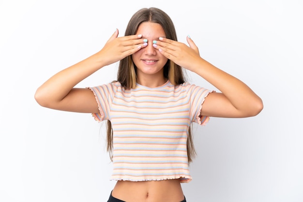 Menina caucasiana isolada no fundo branco, cobrindo os olhos pelas mãos e sorrindo