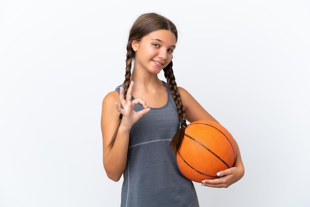 Menina caucasiana isolada no fundo branco jogando basquete e fazendo sinal de OK