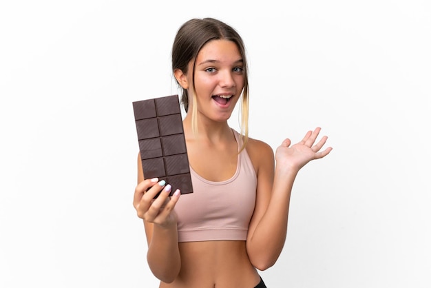 Menina caucasiana isolada no fundo branco tomando uma pastilha de chocolate e surpresa