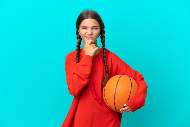 Menina caucasiana jogando basquete isolada em fundo azul com dúvidas e pensando