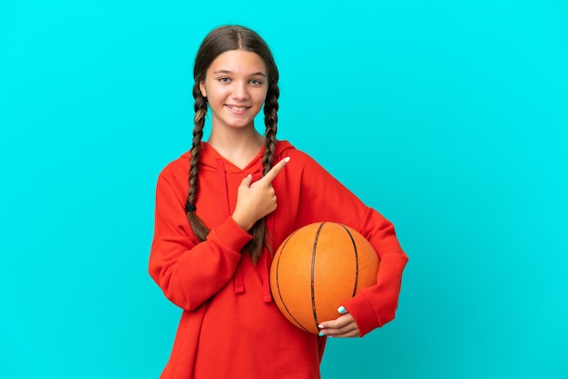 Menina caucasiana jogando basquete isolada em um fundo azul apontando para o lado para apresentar um produto