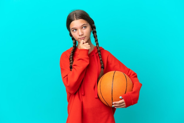 Menina caucasiana jogando basquete isolada em um fundo azul e olhando para cima