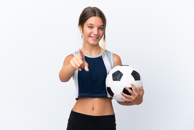 Menina caucasiana jogando futebol isolado no fundo branco surpresa e apontando para a frente