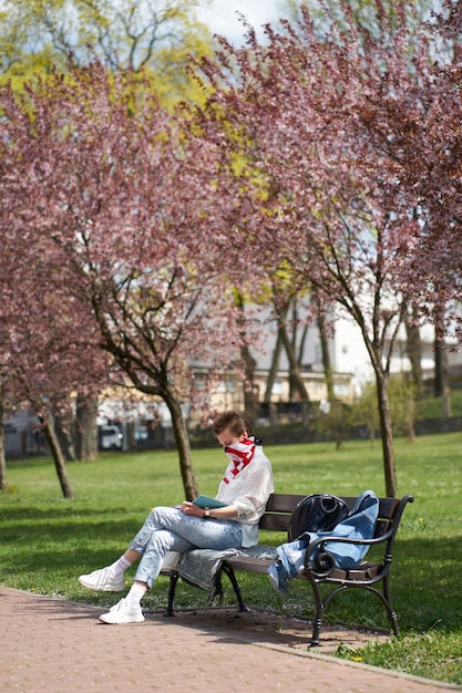 Menina caucasiana, lendo um livro no banco no parque, protegendo o rosto usando bandagem da bandeira americana durante o surto