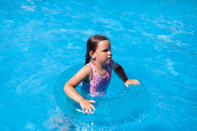 Menina caucasiana molhada pula e se diverte na piscina do hotel em um dia quente e ensolarado