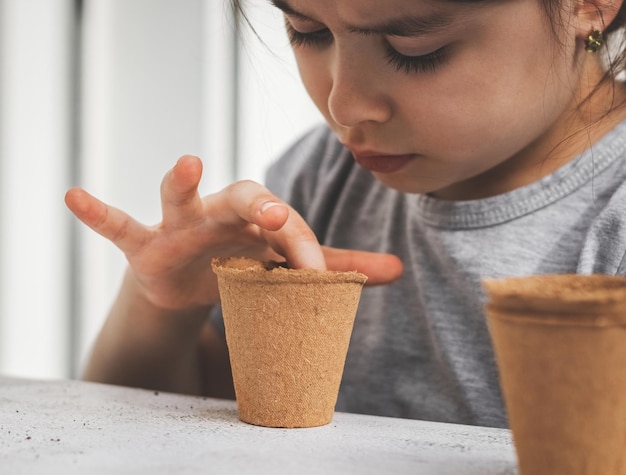 Menina caucasiana plantando sementes em um copo de papelão empurrando o dedo