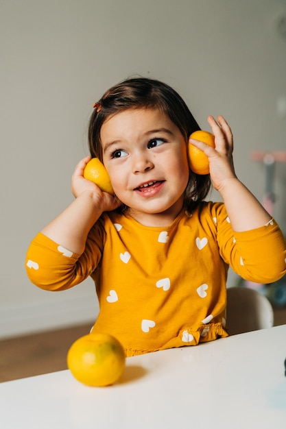 Menina caucasiana se divertindo com tangerinas. Dieta de criança saudável. Reforço imunológico com vitamina c. Foto de alta qualidade