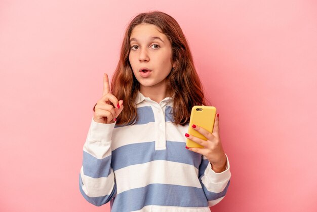 Menina caucasiana, segurando o telefone móvel isolado no fundo rosa, tendo uma ótima ideia, o conceito de criatividade.