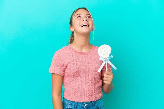 Menina caucasiana segurando um pirulito isolado em um fundo azul rindo