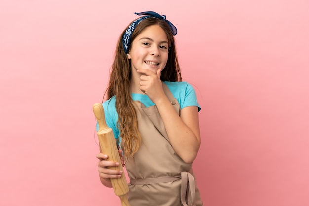 Menina caucasiana segurando um rolo de massa isolada no fundo rosa feliz e sorridente