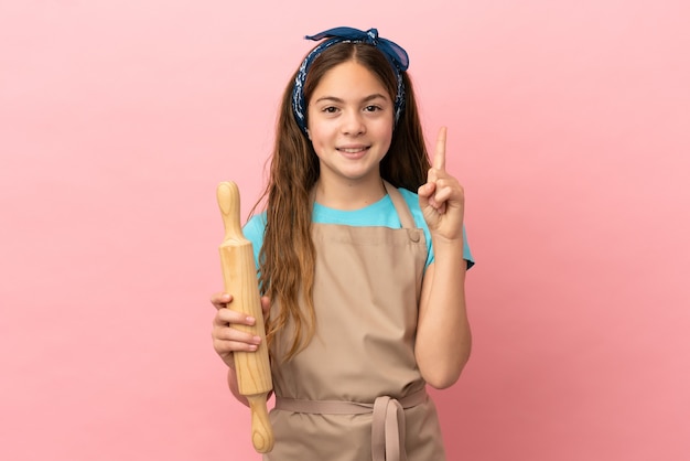 Menina caucasiana segurando um rolo de massa isolado em um fundo rosa apontando para uma ótima ideia